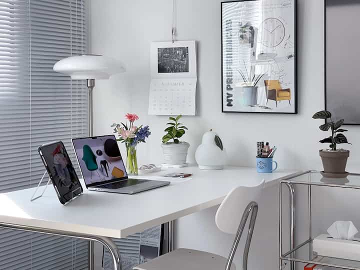 明るい白色調のホームオフィス、白いデスクにノートパソコン、タブレットと植物が配置された清潔感のある作業空間