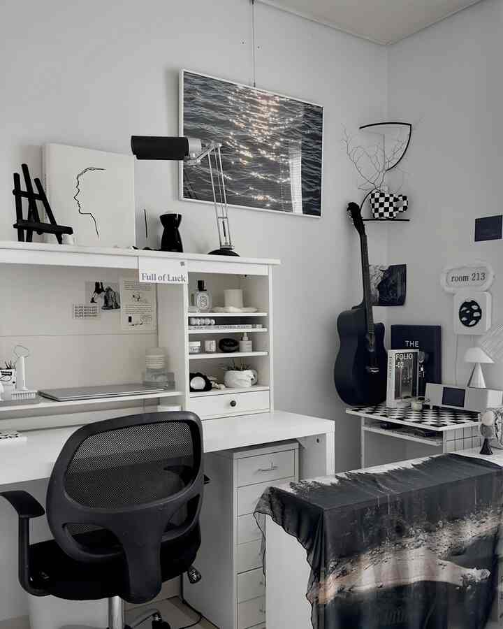 Monotone home office space featuring a white desk, black office chair, posters on walls, and a guitar placed neatly in a clean workspace