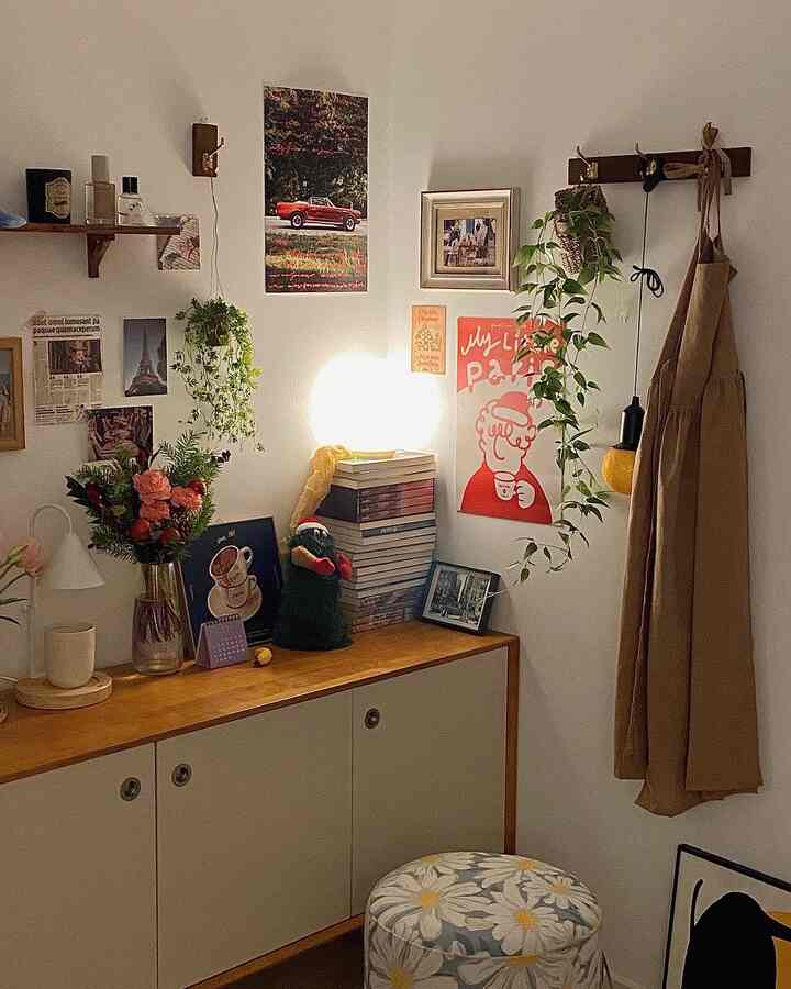 Cozy natural wood tone vintage corner featuring a coat rack with hanging plants, desk with stacked books and warm lighting in a small study/home cafe area