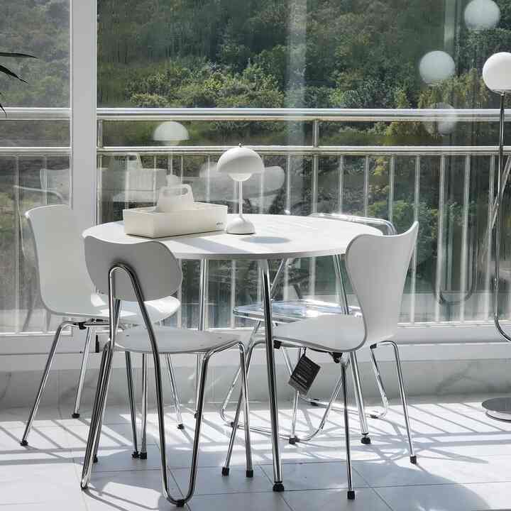 明るい白を基調としたバルコニーの見えるダイニングルーム、丸いダイニングテーブルと椅子、テーブルランプが配置されたモダンな空間