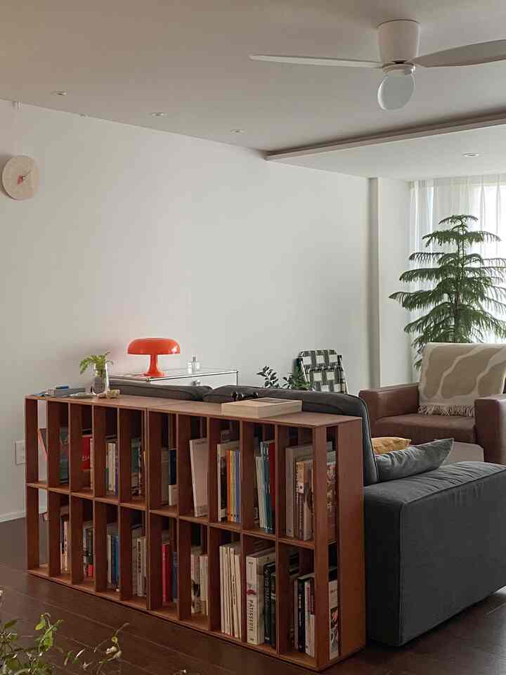 White walls and ceiling backdrop with wooden bookshelf, gray sofa, brown armchair, and orange table lamp in a natural modern living room