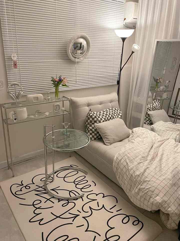 White-toned studio apartment living room featuring a sofa bed, console table, blinds, rug, and large mirror in a cozy setting