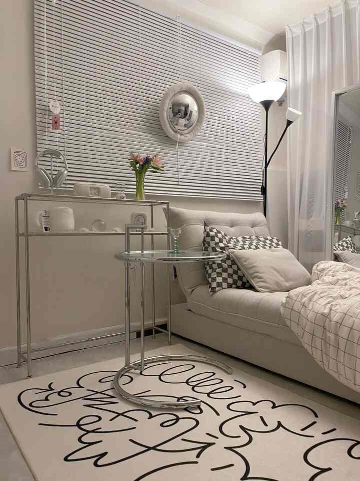 ホワイトトーンのワンルームリビング、メタルとガラスのコンソール・サイドテーブル、柄入りラグ、快適な一人用ソファベッドが調和するモダンなミッドセンチュリースタイルの空間