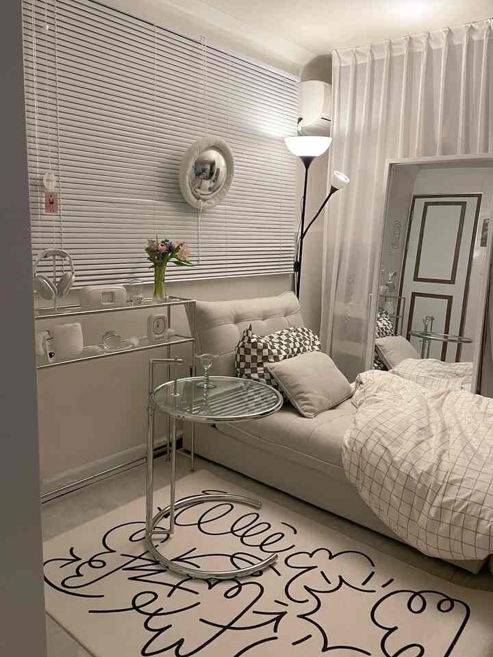 White and beige toned bedroom-living room featuring a sofa bed, blinds, and floor lamp in a modern space