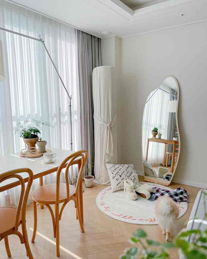 White and wood tone living room featuring wooden dining table and chairs, curtains, and a pet dog with a natural interior vibe
