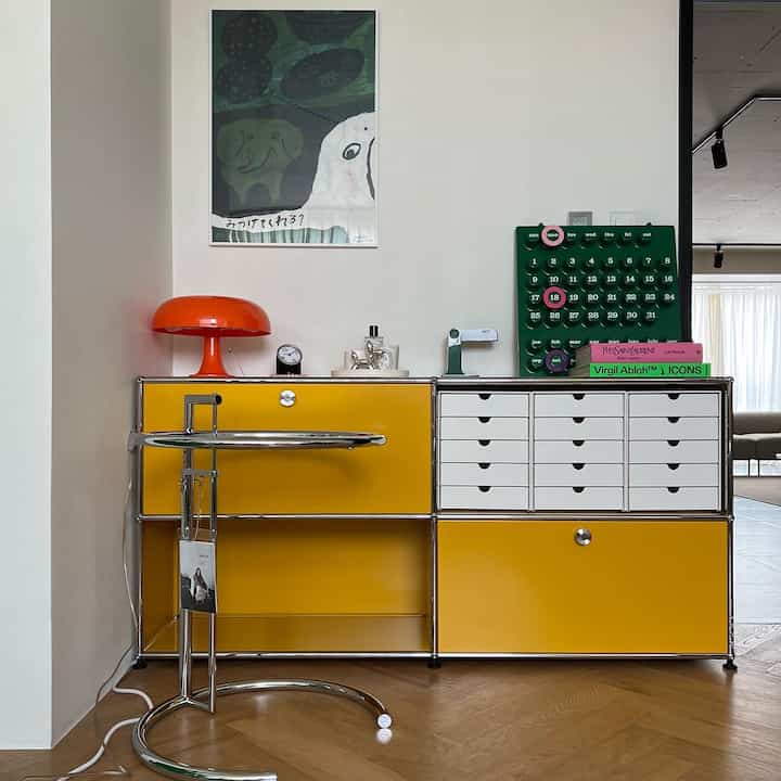 Modern living room featuring yellow and white sideboard with an orange table lamp and books as colorful accents