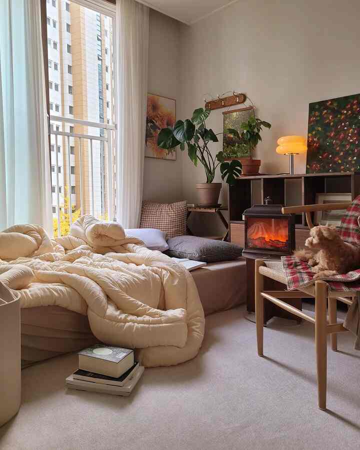 Bright beige natural tone bedroom with cozy bedding, wooden armchair beside sofa, and heater creating a warm ambiance