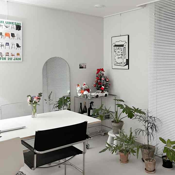 A modern living room in white and black tones featuring a white dining table with chairs centered, plants, and a Christmas tree on the right, creating a neat atmosphere