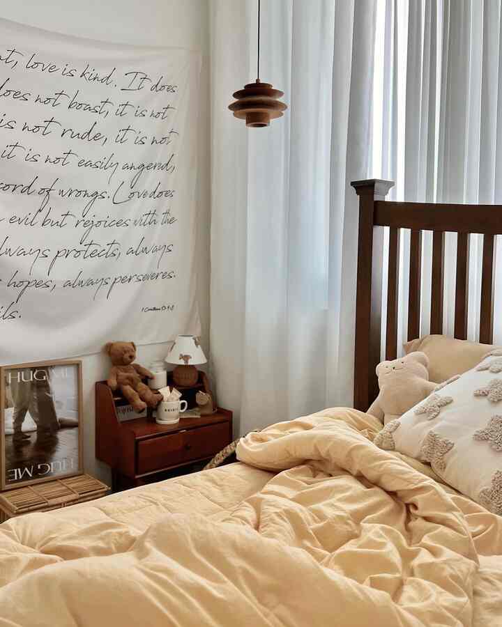 Cozy bedroom space featuring beige bedding, wood tone furniture, and white curtains