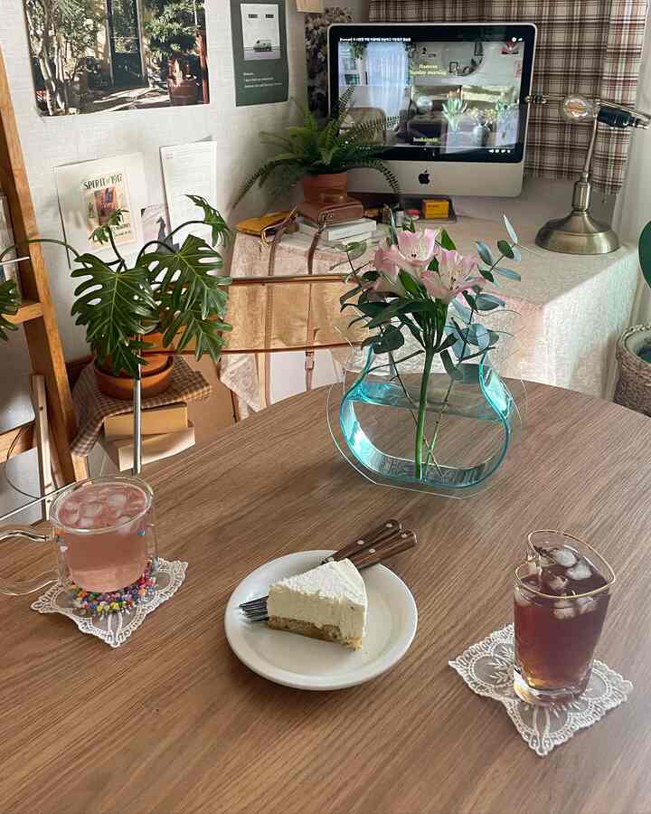 Wood tone and white blended compact home cafe space featuring round dining table with vase, cake, and drinks