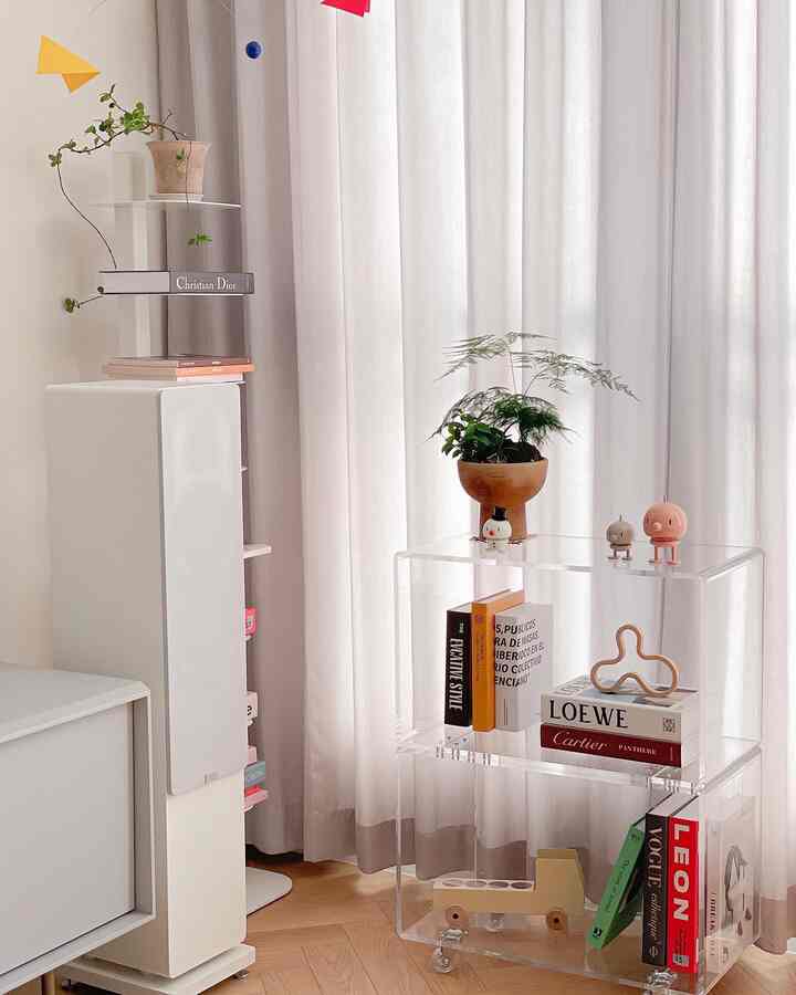 White and natural toned living room featuring transparent shelves, bookshelf, plants, and charming decorative items in a tidy space