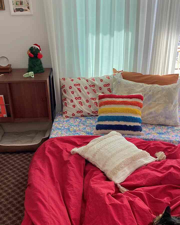 Living room and bedroom with bright mint curtains, vibrant cushions, and a cozy red bedspread