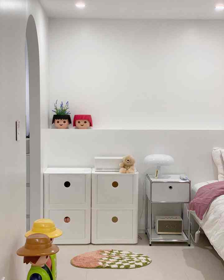 White and beige toned bedroom corner featuring modular storage, nightstand, and cute baby-themed decor in a minimalist and clean style