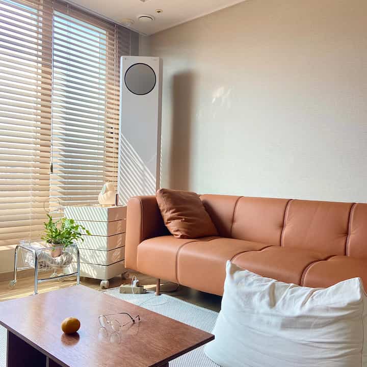 Beige walls and wood-toned furniture grace the living room featuring a brown leather sofa and coffee table in a cozy and clean setting