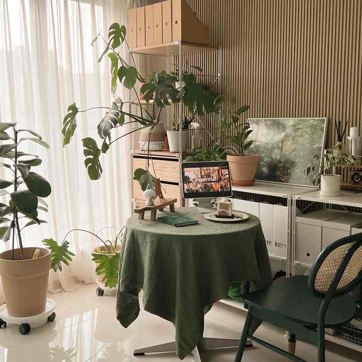 Beige and green toned natural dining space featuring a round table and numerous plants, creating a cozy interior atmosphere