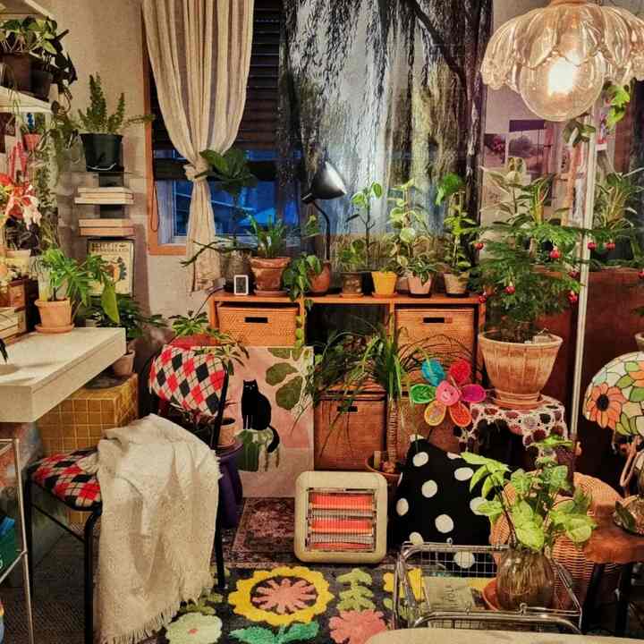 ナチュラルカラーのワンルームリビング、豊富な植物とラタン収納、クッションと暖房器具が調和した温かみのあるインテリア