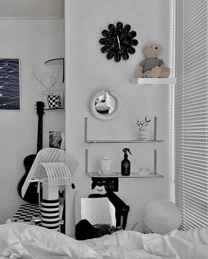 A white and black monotone bedroom space featuring a wall clock, wall shelves, mirrors, and guitar in a modern and clean interior