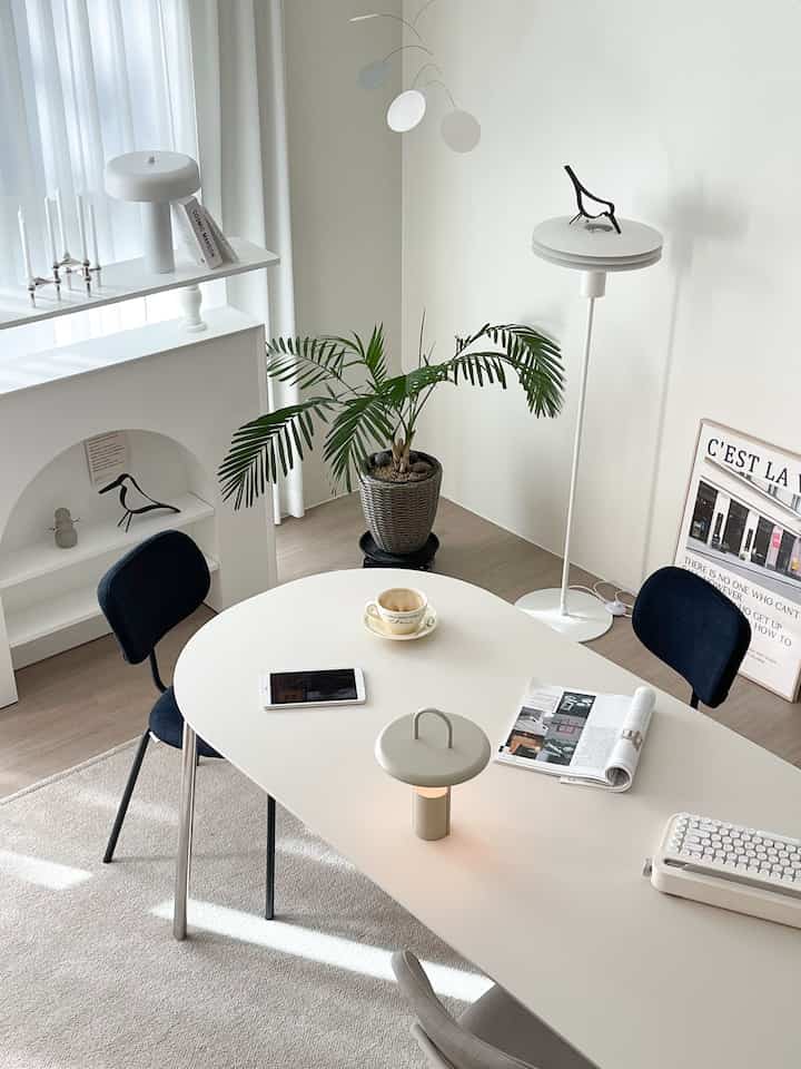 白とナチュラルトーンのリビングルーム、大きなテーブルと青い椅子が配置されており、落ち着いた印象的な空間