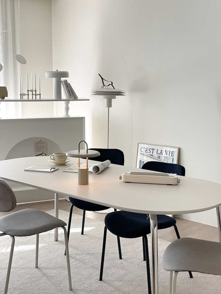 Beige and white toned mid-century modern home office featuring stainless steel oval dining table with assorted chairs