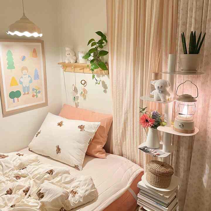 やわらかなピンク色調の寝室、くま柄の布団と木製棚、レトロなムードの照明が配置された印象的な空間