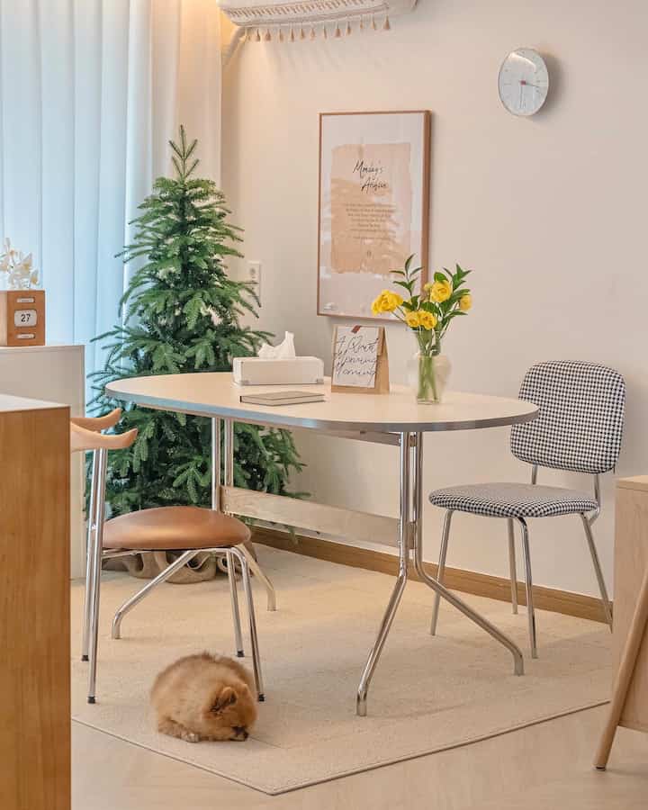 A cozy small dining room in white and wood tones, featuring a Christmas tree and a sleeping dog as accents