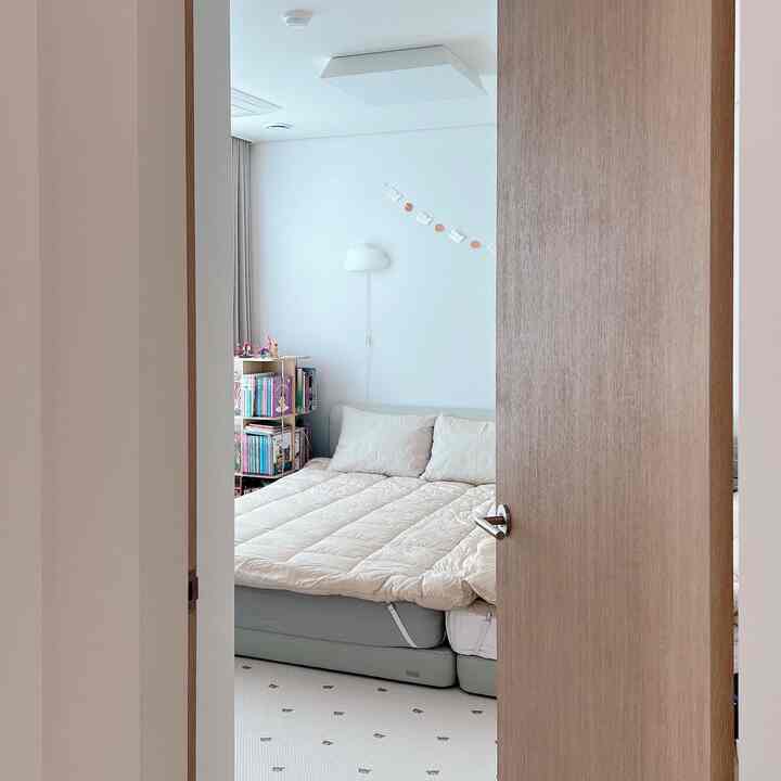 白い壁と木目調のドアがある子供部屋、ベッドと子供用の本棚が配置された清潔感のある柔らかな雰囲気のインテリア