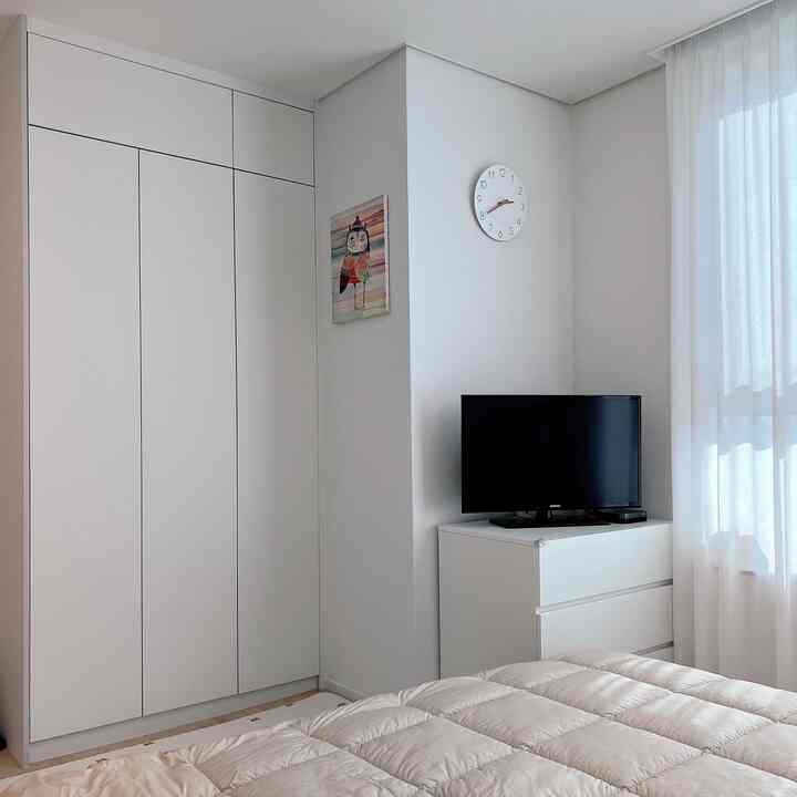 白と木目調の子供部屋、白いチェストと時計、そして透け感のあるカーテンが柔らかな雰囲気を演出するインテリア