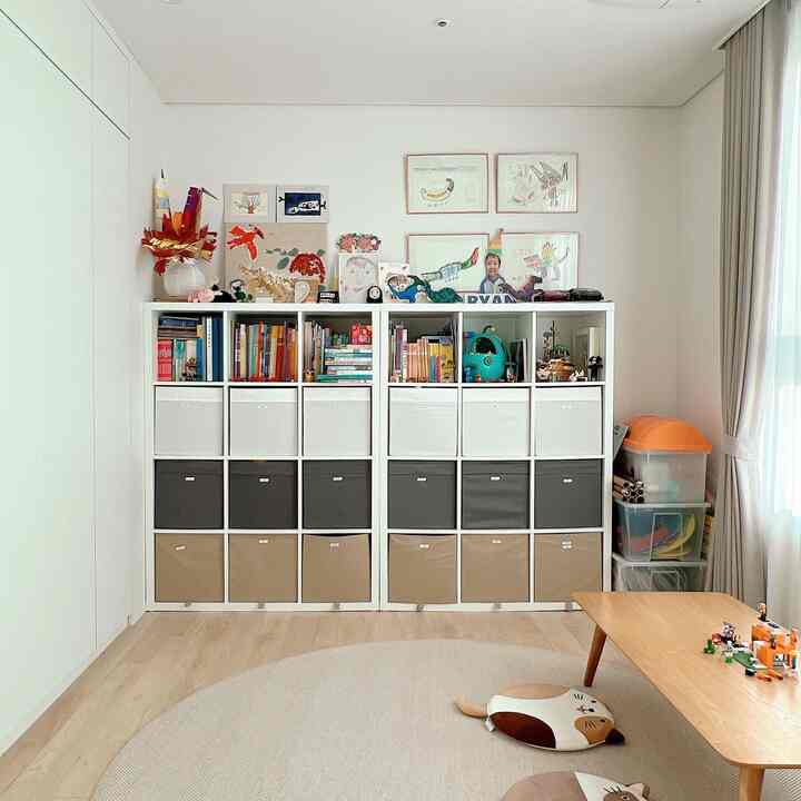 白と木目調が調和した子供部屋、おもちゃ収納棚とラグ、低めのテーブルが配置されたすっきりとした空間