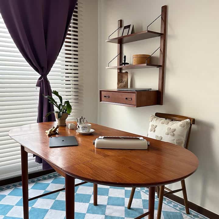 Cozy study featuring deep purple blackout curtains, wood tone desk and wall shelves