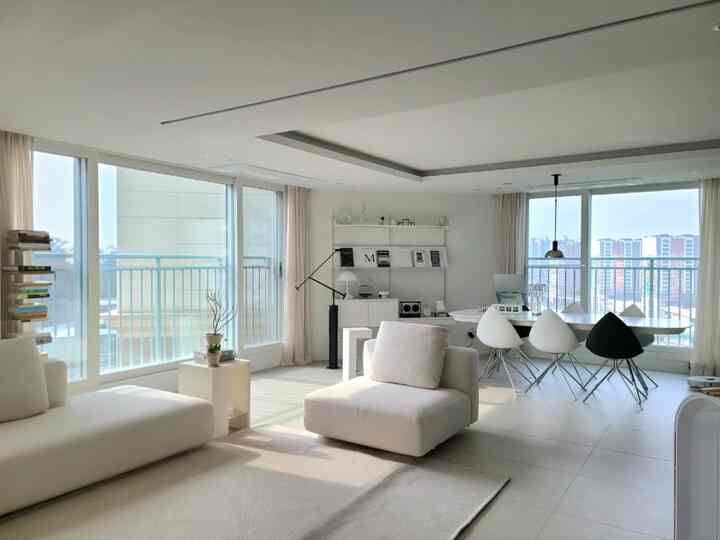 White-tone living room connected to veranda, featuring modern sofas and dining table in a bright and clean space