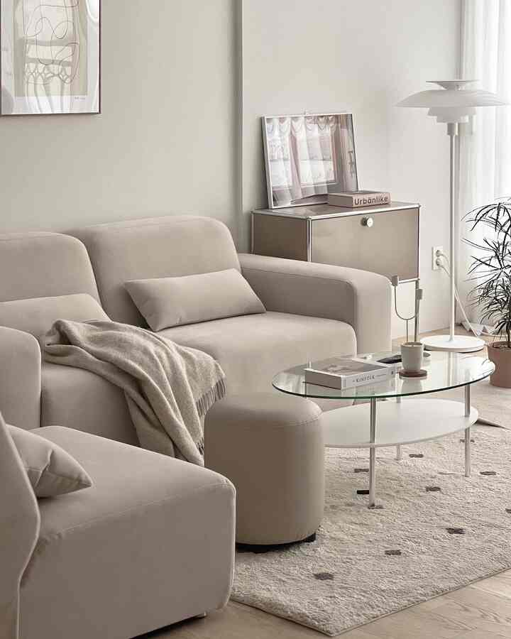 Beige and white tone living room featuring modern sofas, stool, and glass coffee table in a cozy setting
