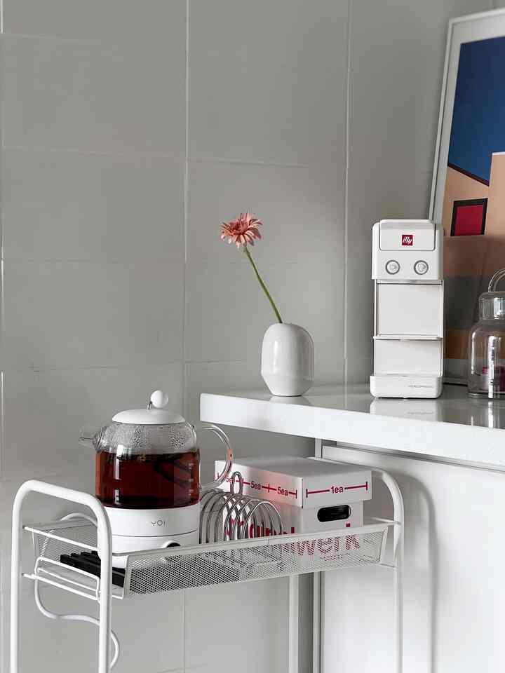 白を基調としたキッチン空間、キッチンワゴンとガラスの電気ケトル、コーヒーマシンが配置されたミニマルなインテリア