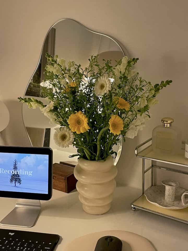 白を基調としたホームオフィス、中央に配置されたクリーム色の花瓶と黄色い花が印象的な空間