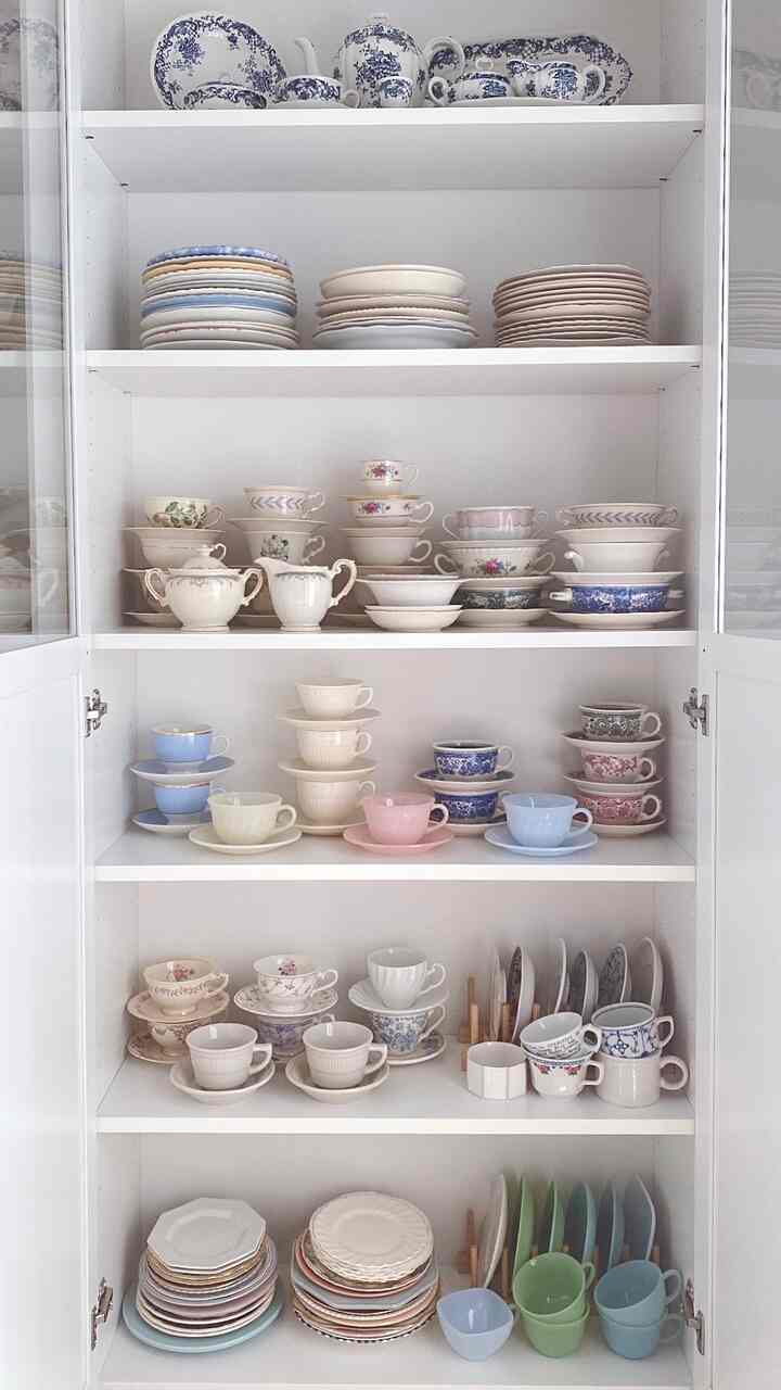 白を基調としたキッチン収納キャビネットにヴィンテージ風のティーカップと皿が整然と並んだ雰囲気のあるインテリア
