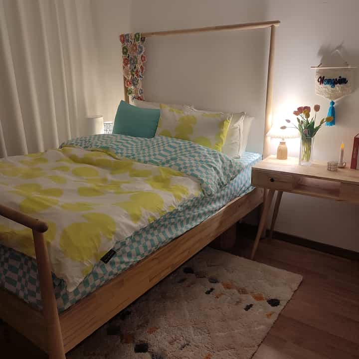 A white and mint toned bedroom featuring a wooden bed and console table with floral decorations and cozy lighting