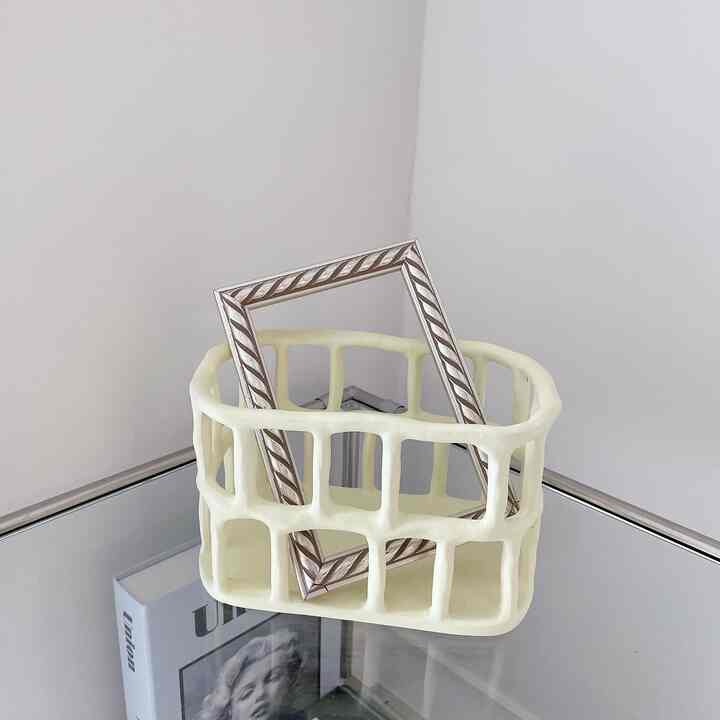 Minimal interior element featuring a vintage picture frame placed inside a butter color basket on a mirrored surface