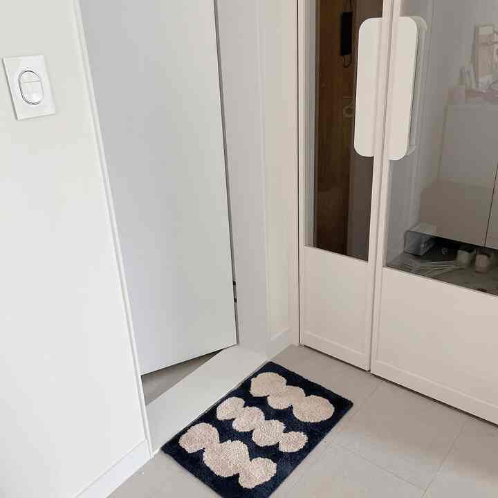 白を基調とした狭い玄関、ネイビーとベージュのバスマットが配置された清潔感のある空間
