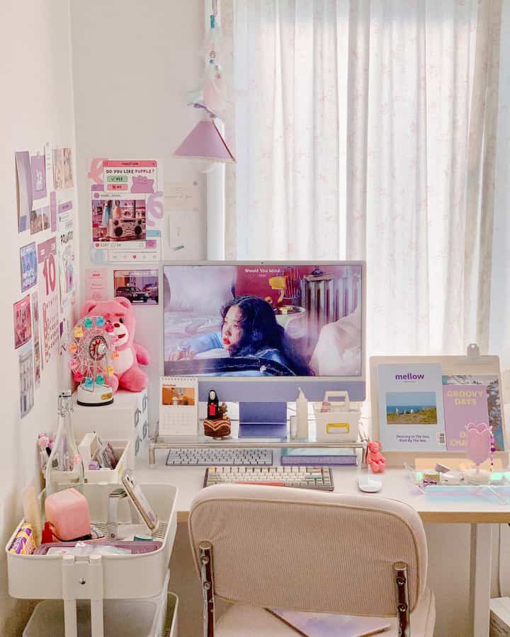 A compact home office space in white and pink tones featuring a desk with monitor stand and various cute accessories arranged neatly
