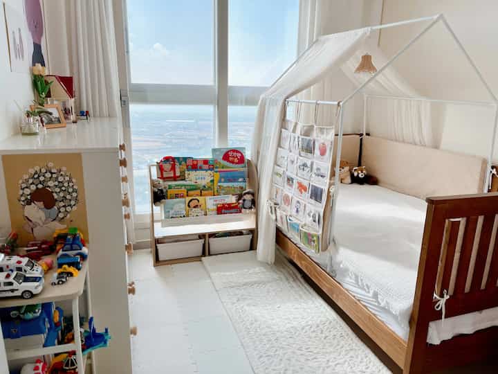 A white and brown toned kids' room featuring a wooden daybed, children's bookshelf, and toy storage creating a cozy and neat space