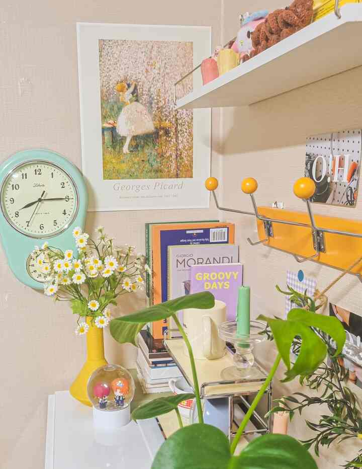 Cozy corner featuring a yellow and mint toned nightstand with a clock, poster, candle, and plants