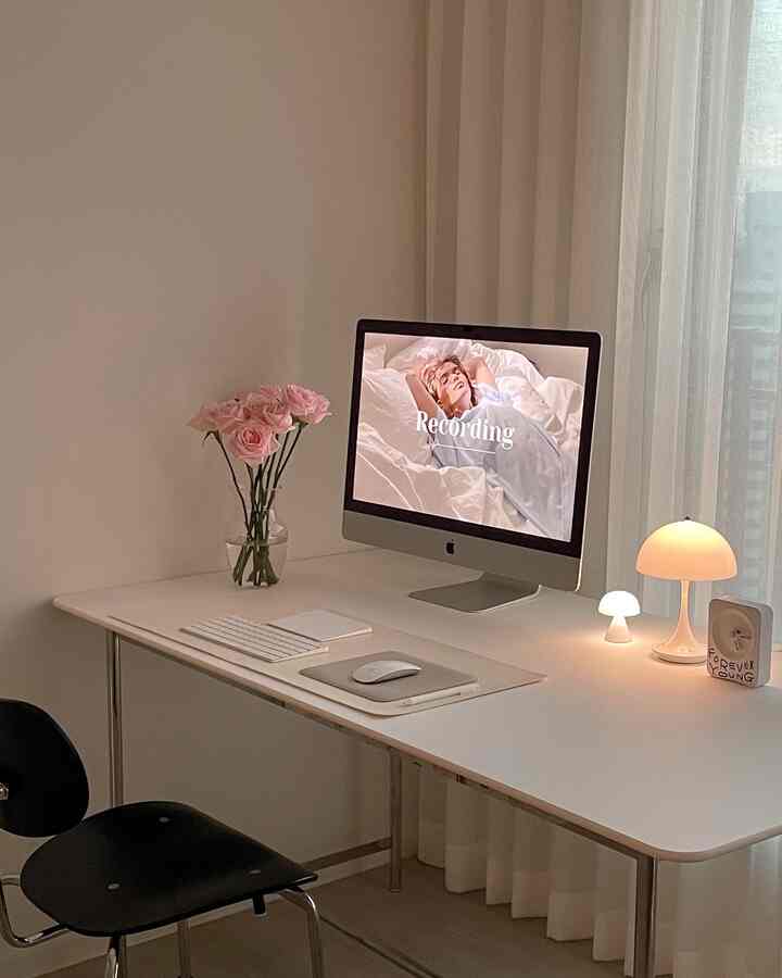 Minimal modern home office space in white and black tones, with computer, pink rose vase, and table lamps on the desk, creating a cozy atmosphere