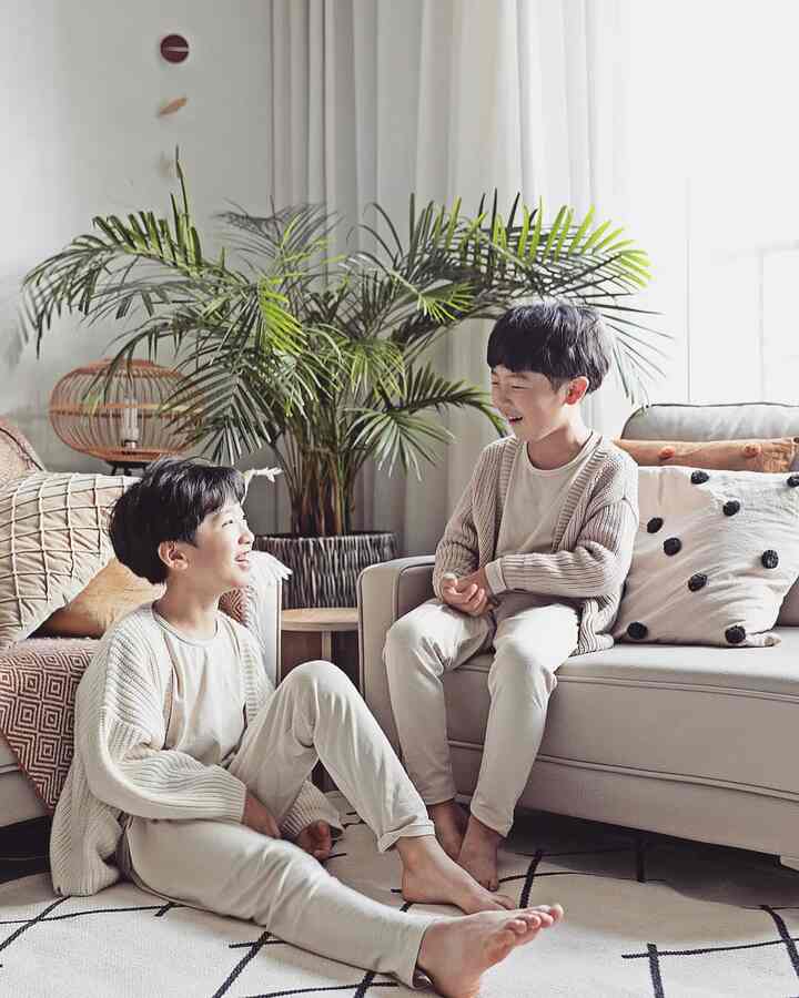 ベージュとホワイトの自然な色調のリビングルーム、子供たちが遊び、大きなアレカヤシの植物が空間に活気を与える印象的な空間