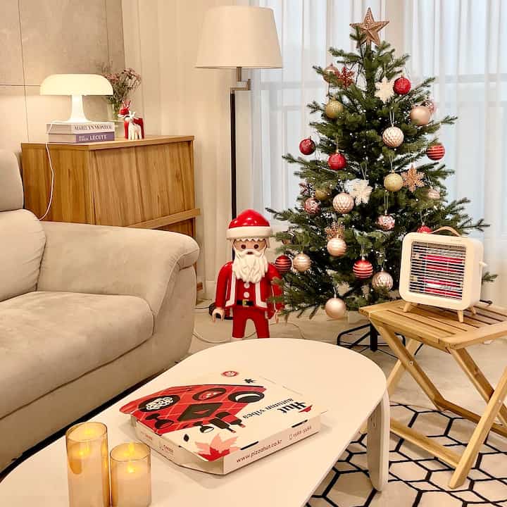 White and beige toned living room featuring a Christmas tree, large Playmobil Santa figure, sofa, and mini heater creating a cozy atmosphere