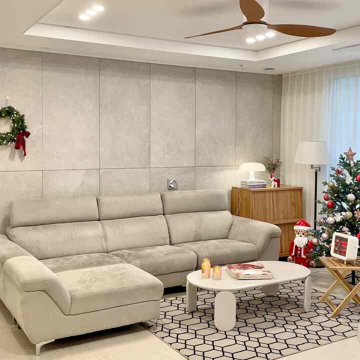 Bright beige and wood-toned living room featuring large sectional sofa, Christmas tree, small stool, and floor lamp with cozy winter atmosphere