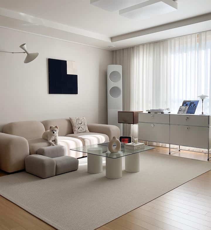 A beige and white-toned living room featuring a modern sofa and glass coffee table with a cozy atmosphere