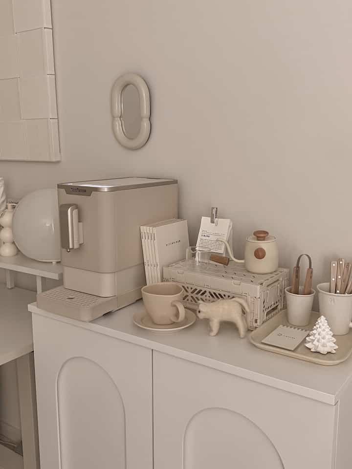 Bright white and beige toned home cafe space featuring coffee machine, mugs, and tray arranged neatly