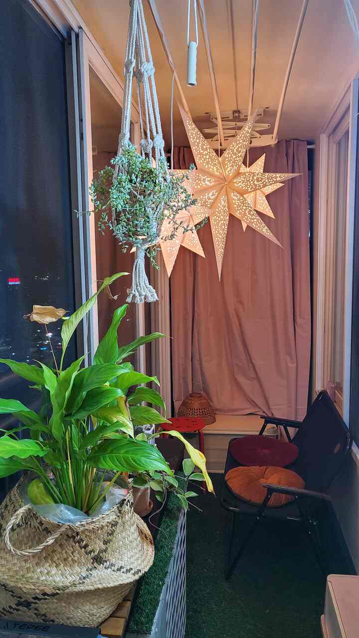 Natural green and brown toned veranda with various plants and star-shaped pendant lights creating a cozy atmosphere