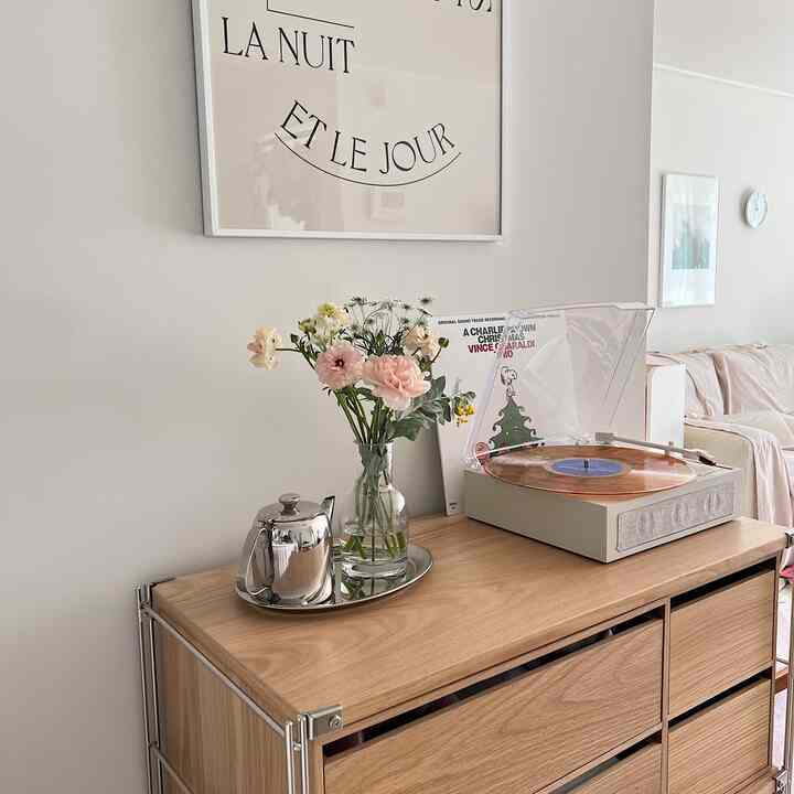 ベージュと木目調のリビングキッチン空間、木製キャビネットの上にLPプレーヤーと花瓶、ティーポットが配置されたナチュラルモダンなインテリア