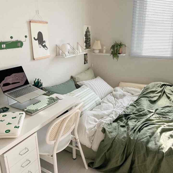 ホワイトとグリーンの色調の小さな寝室で、デスクとベッドリネンが配置された自然でシンプルな印象的なホームオフィス空間