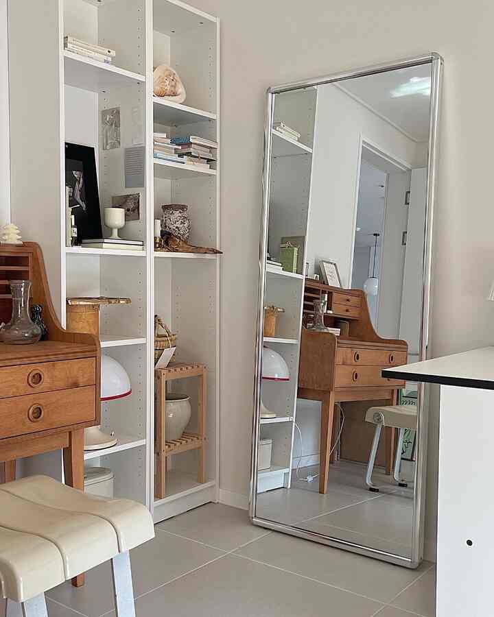 White and brown toned study featuring a large full-length mirror and mid-century modern wooden desk with a clean, cozy atmosphere